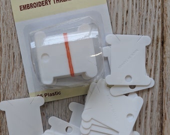 Könnte beinhalten: Eine Packung mit 25 weißen Plastik-Stickgarn-Spulen. Die Verpackung ist mit "Siesta Embroidery Thread Bobbins" beschriftet.