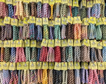 May include: A wall display of colorful embroidery floss spools, each with a yellow label featuring the brand name "DMC" and a number. The floss is arranged in rows, creating a vibrant and organized display.