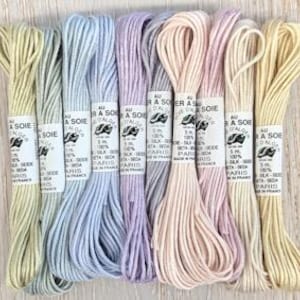 May include: Eight spools of pale pink, lavender, light blue, and cream coloured embroidery floss. Each spool is labelled "Au fil a Soie" and "Dalo Paris".
