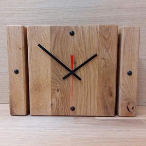 Könnte beinhalten: Eine quadratische Holzuhr mit schwarzen Zeigern und einem roten Sekundenzeiger. Die Uhr ist aus recyceltem Holz gefertigt und hat einen rustikalen Look.