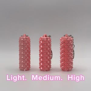 K&ouml;nnte beinhalten: Drei zylindrische, rosafarbene Schl&uuml;sselanh&auml;nger mit einer texturierten, stacheligen Oberfl&auml;che. Jeder Schl&uuml;sselanh&auml;nger hat oben einen Metallring. Der Text "Light. Medium. High" ist unten in Wei&szlig; aufgedruckt und entspricht den drei gezeigten Artikeln.