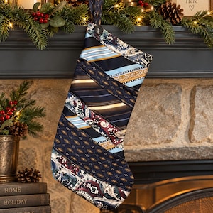Puede incluir: Un calcetín navideño confeccionado con varias corbatas que presenta un mosaico de rayas diagonales, estampados de cachemira y motivos geométricos en tonos azul marino, azul claro, dorado, blanco y burdeos, con un botón negro.