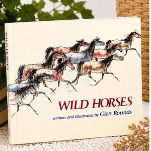 May include: A hardcover book titled "Wild Horses" with a cream-colored cover. The cover features a drawing of several horses in motion, with text in red and blue. The book is written and illustrated by Glen Rounds.