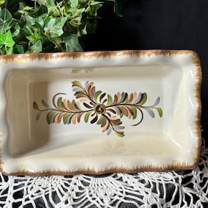 Puede incluir: Fuente rectangular de cerámica color crema con borde festoneado y borde marrón. La fuente presenta un diseño floral central en tonos marrón, verde y azul. Artículos de cocina decorativos.