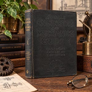 May include: A black, vintage hardcover book titled Audels Engineers and Mechanics Guide 1, featuring embossed text on the front cover and spine. The cover includes the phrase Questions Answers and Illustrations and a sun icon with the text Look Within.
