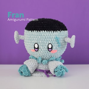 May include: Fran Amigurumi Pattern crochet doll with a blue and black body, purple ribbon, and pink cheeks.