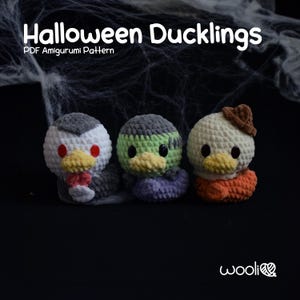 May include: Three crocheted Halloween ducklings. The ducklings are dressed as a vampire, Frankenstein, and a witch. The ducklings are sitting on a black background with a spider web.