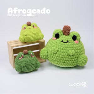 Puede incluir: Tres peluches de rana de ganchillo de diferentes tamaños, con el texto "Afrogcado PDF Amigurumi Pattern". Las ranas son verdes con ojos negros, mejillas rosas y una parte superior marrón. Los peluches se muestran sobre un fondo claro.
