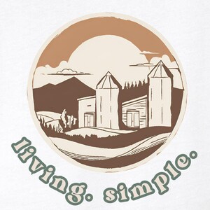 Peut inclure: T-shirt blanc avec un graphique circulaire brun représentant une scène de ferme avec un soleil, des montagnes et deux granges. Le texte "living. simple." est écrit en vert sous le cercle.