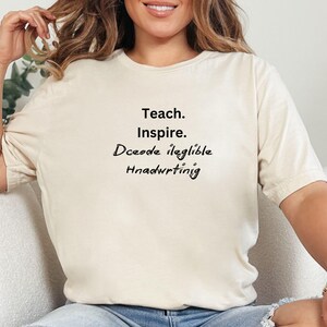 Puede incluir: Una camiseta blanca con el texto "Teach. Inspire. Decode illegible handwriting" impreso en la parte delantera.