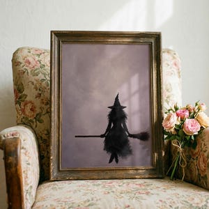 Könnte beinhalten: Ein gerahmter Kunstdruck mit der dunklen Silhouette einer Hexe mit spitzem Hut, die auf einem Besenstiel vor einem gedämpften, wolkigen violetten Hintergrund reitet. Der rechteckige Rahmen besteht aus dunklem Holz mit sichtbarer Maserung.