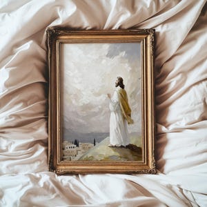 Pu&ograve; includere: Un dipinto a olio incorniciato raffigurante una figura con una veste bianca e uno scialle dorato, in piedi su una collina che si affaccia su una citt&agrave;. La figura guarda verso un cielo luminoso e nuvoloso con le mani giunte, in una cornice dorata.
