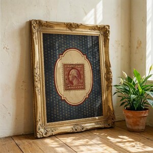 Op de afbeelding: Een ingelijste vintage postzegel met George Washington. De postzegel is rood en cr&egrave;mekleurig, tegen een marineblauwe achtergrond met gouden steraccenten. De sierlijke gouden lijst voegt een klassieke touch toe aan het kunstwerk.