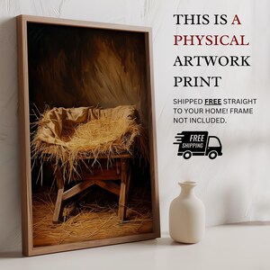 May include: A framed artwork print depicting a manger scene with straw and a cloth. The print is in a wooden frame. Text on the image reads "THIS IS A PHYSICAL ARTWORK PRINT" and "SHIPPED FREE STRAIGHT TO YOUR HOME! FRAME NOT INCLUDED."