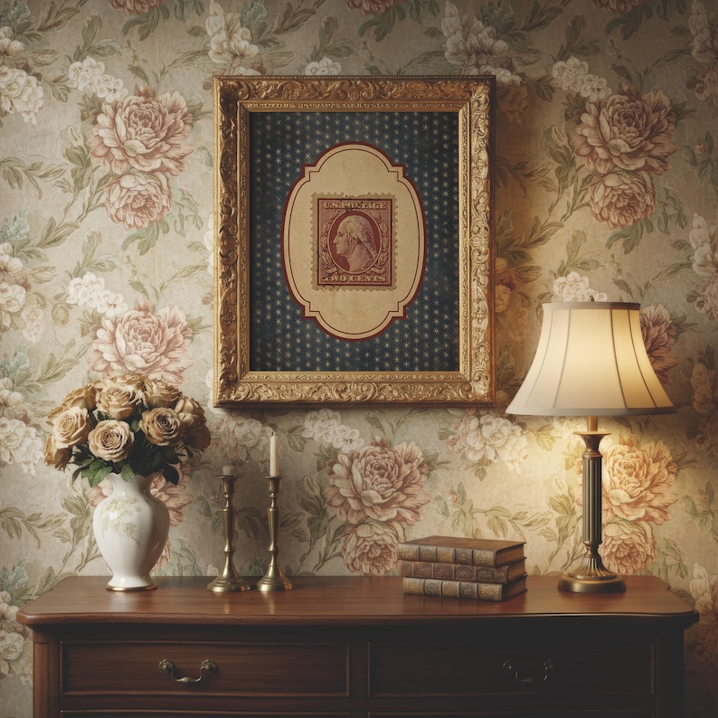 Op de afbeelding: Een ingelijst vintage postzegelkunstwerk met een gouden lijst, met een portret van George Washington. Het kunstwerk hangt boven een houten tafel met een lamp, boeken en een vaas met bloemen. Het behang heeft een bloemenpatroon.