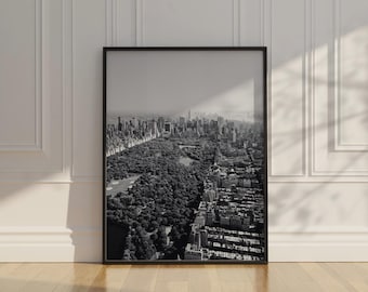 May include: Black and white framed aerial photograph of a city with a large park. The photograph captures a sprawling urban landscape with tall buildings and a prominent green space, likely Central Park.
