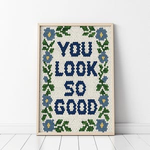 Puede incluir: Impresi&oacute;n art&iacute;stica enmarcada con las palabras "YOU LOOK SO GOOD" en azul marino, rodeada por un borde floral de flores azules y hojas verdes. El fondo es un patr&oacute;n de mosaico. El marco es de color madera clara.