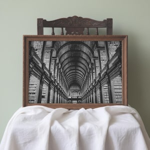 May include: A rectangular framed wall art piece featuring a black and white photograph of a long library hall with a high arched ceiling and tall wooden bookshelves lining both sides, encased in a dark brown ornate wooden frame with a carved top.