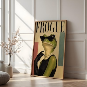 May include: A framed wall art print featuring a green frog wearing black cat-eye sunglasses, a multi-strand pearl necklace, and a black sleeveless top with matching black gloves. The text FROGUE is printed in large black letters at the top.