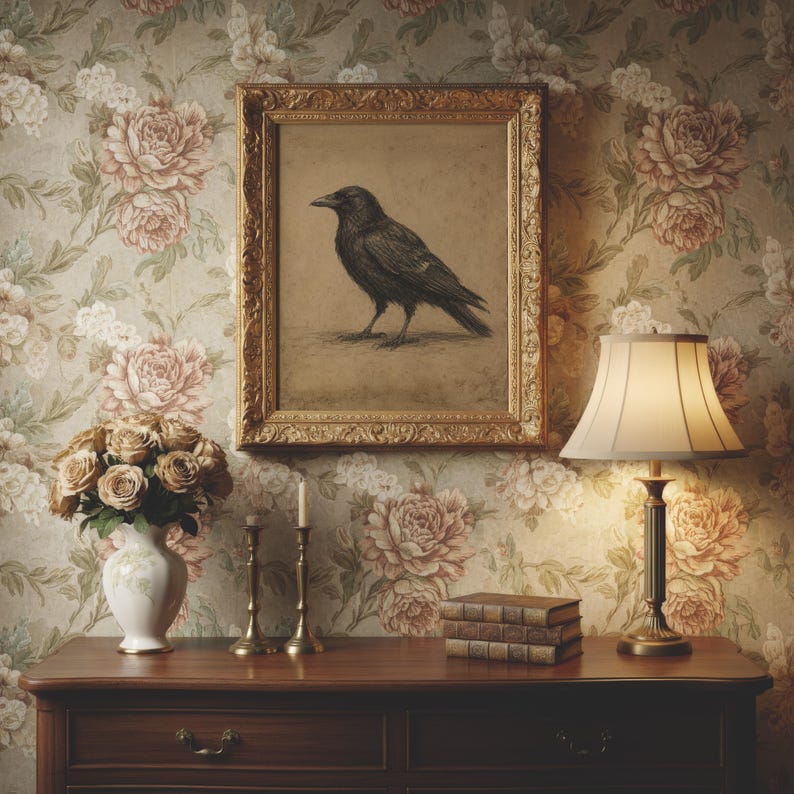 May include: A framed charcoal drawing of a black crow hangs above a wooden dresser. The dresser holds a white vase with beige roses, two brass candlesticks, a stack of three leather-bound books, and a table lamp with a cream-colored shade.
