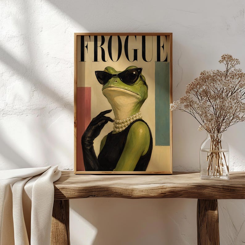 May include: A framed wall art print featuring a green frog wearing black sunglasses, a black sleeveless top, and a multi-strand pearl necklace. The frog is wearing a black glove on one hand. The text FROGUE is printed in large black letters at the top.