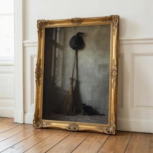 May include: A large, ornate gold-toned rectangular frame containing a print of a black pointed hat hanging above a wooden broomstick, with a small black cat sitting on the floor beside the broom, all set against a muted grey wall background.