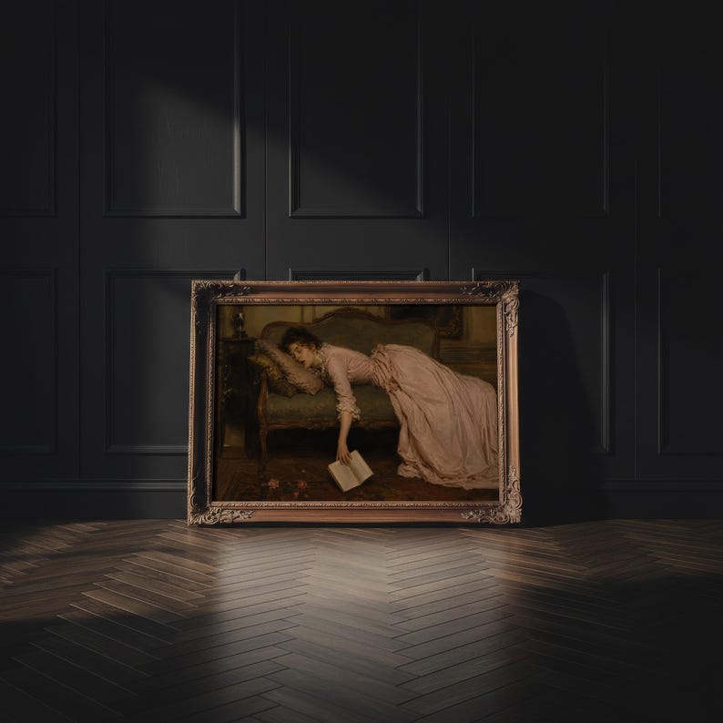 May include: A framed oil painting depicting a person in a long, pale pink dress reclining on a dark upholstered sofa. The person is asleep with one hand hanging down, holding an open book. The painting is enclosed in an ornate, dark gold frame.