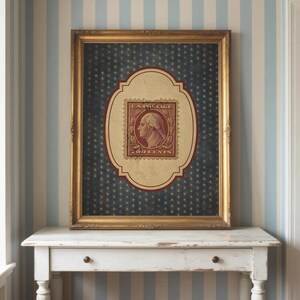 Op de afbeelding: Ingelijste vintage Amerikaanse postzegelkunst. Het kunstwerk heeft een gouden lijst, een donkerblauwe achtergrond met een sterrenpatroon en een centraal ovaal met een rode en cr&egrave;mekleurige postzegel. De postzegel toont George Washington en luidt "U.S. Postage Two Cents."