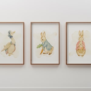 May include: Three framed watercolor prints featuring characters from a children's story. The prints depict a goose in a bonnet, a rabbit holding a carrot and greens, and a rabbit with a basket. The frames are brown.