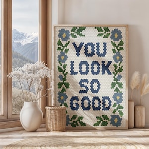 Puede incluir: Un cuadro enmarcado con las palabras "YOU LOOK SO GOOD" en letras de mosaico azul. La obra de arte est&aacute; rodeada por un borde floral de mosaicos azules y verdes. La impresi&oacute;n se exhibe en una habitaci&oacute;n con una ventana que da a una cordillera.