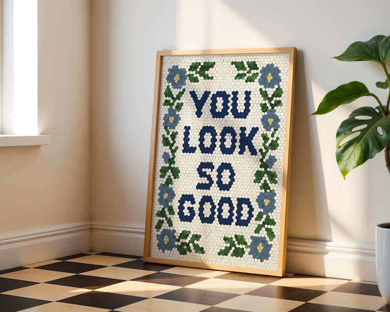 Puede incluir: Un cuadro enmarcado con la frase "YOU LOOK SO GOOD" en azul marino, rodeado por un borde floral azul y verde. La obra de arte tiene un efecto de mosaico y est&aacute; enmarcada en un marco de madera clara.