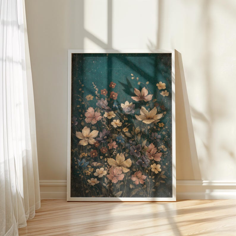 May include: A framed floral print featuring a variety of flowers in shades of yellow, pink, and purple against a dark teal background. The artwork is displayed on a wooden floor, with sunlight casting shadows from a nearby window.