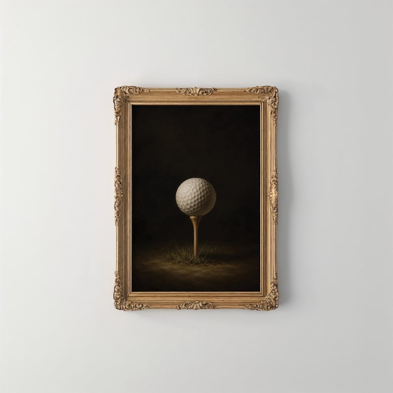 Op de afbeelding: Een witte golfbal staat op een houten tee in een plukje gras, gecentreerd tegen een donkere achtergrond. Het geheel is gevat in een sierlijke, rechthoekige goudkleurige lijst met gedetailleerd houtsnijwerk langs de randen.