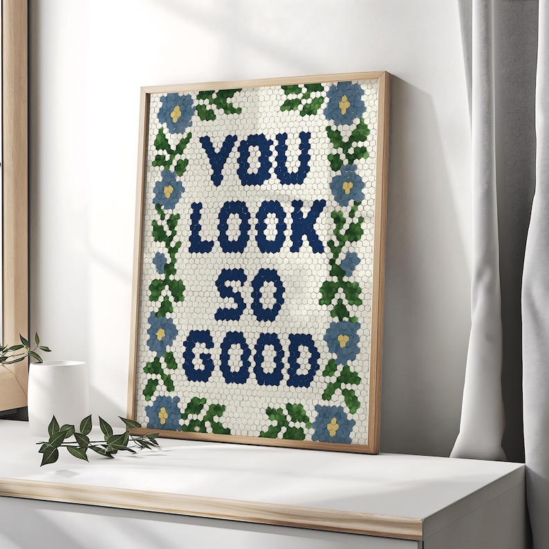 Puede incluir: Obra de arte enmarcada con el texto "YOU LOOK SO GOOD" en letras hexagonales azul marino. La obra est&aacute; rodeada por un borde floral con flores azules y hojas verdes. El marco es de color marr&oacute;n claro.