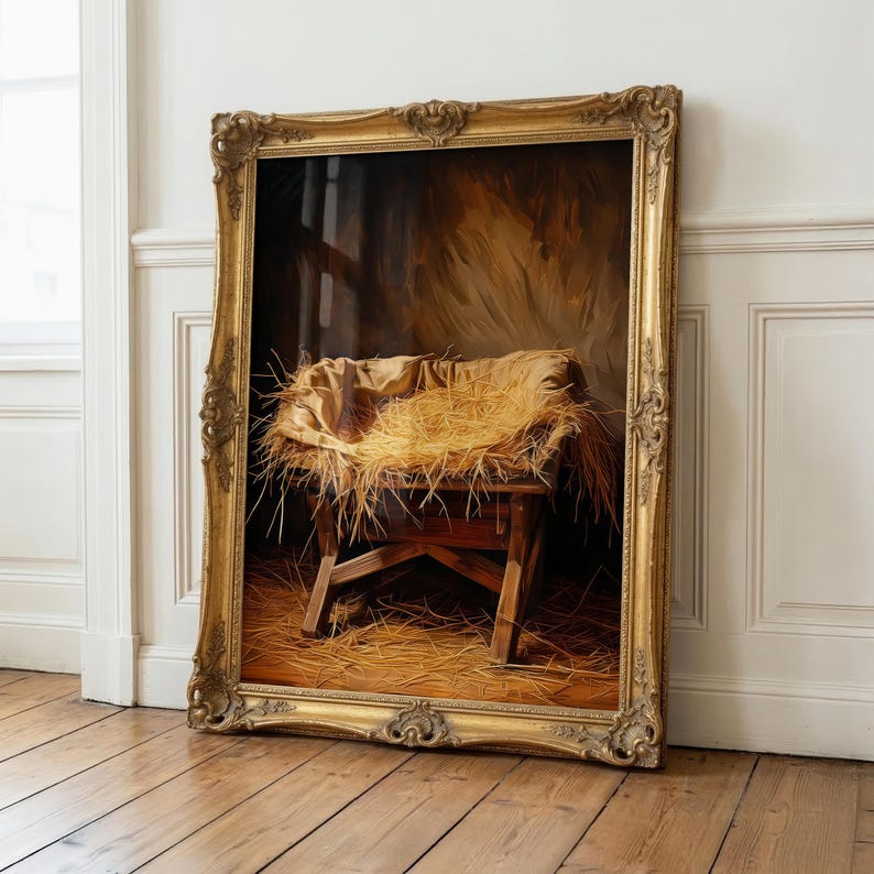 May include: A framed painting depicts a wooden manger filled with straw, set against a backdrop of a dimly lit stable. The painting is encased in an ornate, gold-colored frame, leaning against a white wall and wooden floor.