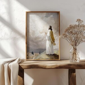 Pu&ograve; includere: Una stampa artistica da parete incorniciata che raffigura una figura con una veste bianca e uno scialle color marrone chiaro su una collina che si affaccia su una citt&agrave; di pietra. Il cielo nuvoloso e luminoso mostra pennellate in toni neutri.