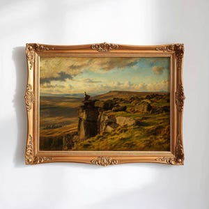 Puede incluir: Una pintura de paisaje antigua en un marco dorado y ornamentado. La obra representa a una persona sentada en un acantilado con vistas a un vasto paisaje cubierto de hierba bajo un cielo nublado. El marco tiene detalles de volutas.