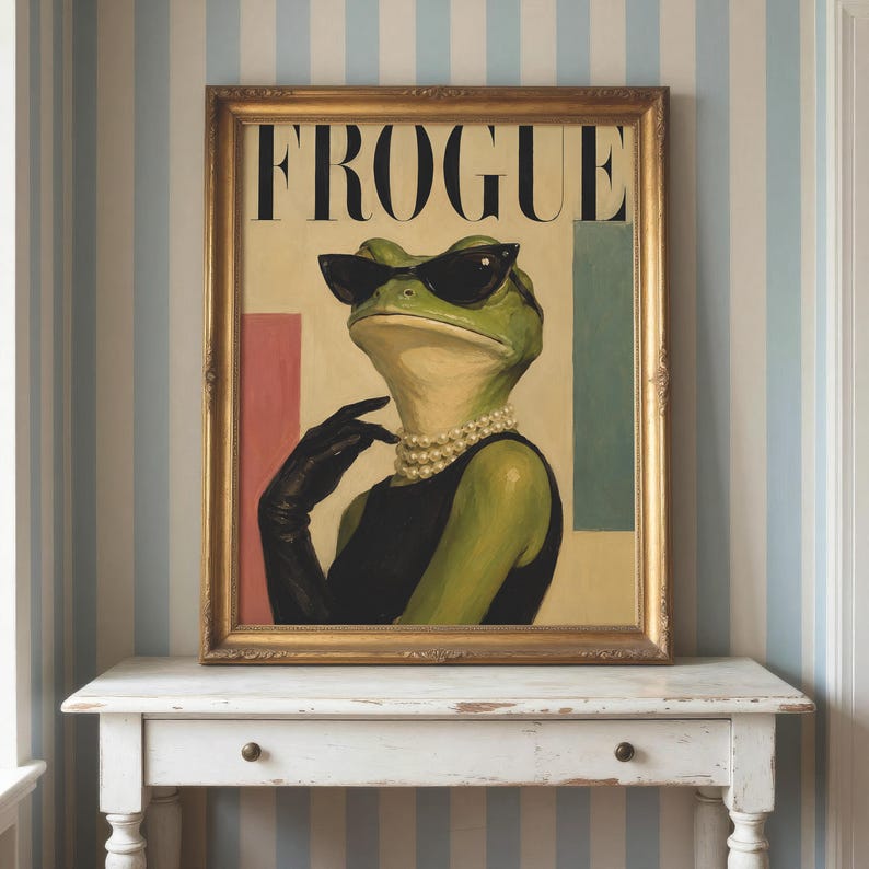 May include: A framed wall art print featuring a green frog wearing black cat-eye sunglasses, a black sleeveless top, black gloves, and a multi-strand pearl necklace. The word FROGUE is printed in large black capital letters at the top of the image.