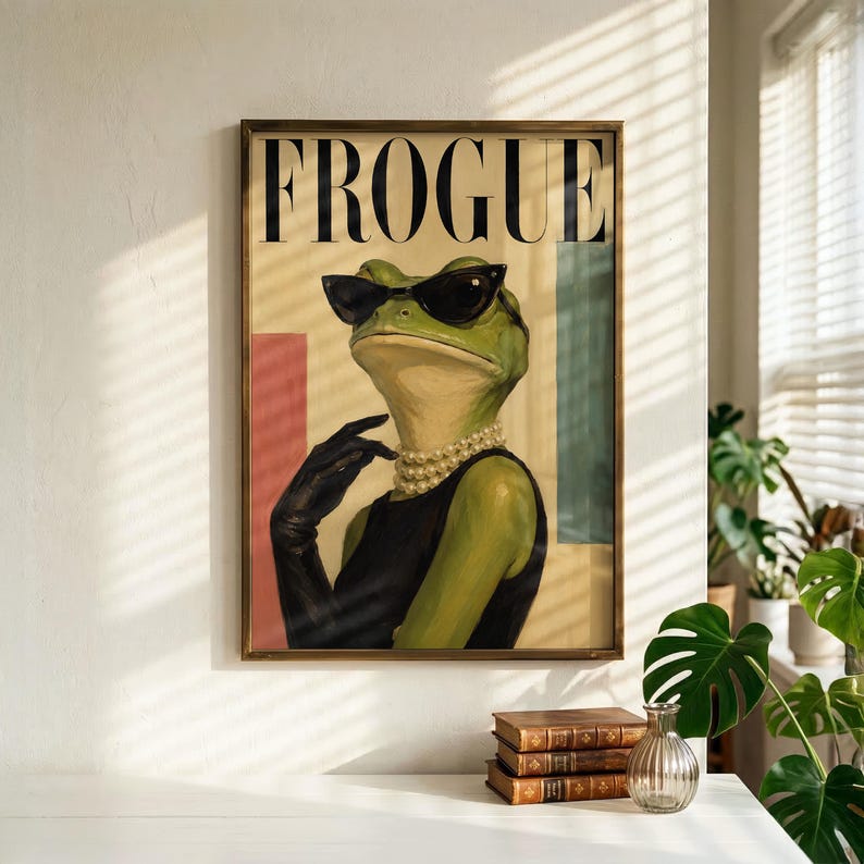 May include: A framed wall art print featuring a green frog wearing black cat-eye sunglasses, a multi-strand pearl necklace, and a black sleeveless top with a black glove. The text FROGUE is printed in large black serif letters at the top.