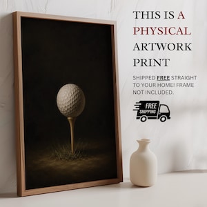 Op de afbeelding: Een ingelijste kunstdruk met een witte golfbal op een houten tee tegen een donkere achtergrond. De tekst luidt: THIS IS A PHYSICAL ARTWORK PRINT. SHIPPED FREE STRAIGHT TO YOUR HOME! FRAME NOT INCLUDED. Een kleine witte vaas staat ernaast.