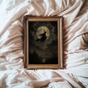 May include: A rectangular wall art piece in an ornate gold frame featuring a dark, atmospheric illustration of a silhouette of a witch flying on a broomstick against a large, glowing full moon, with a castle and dark clouds in the background.