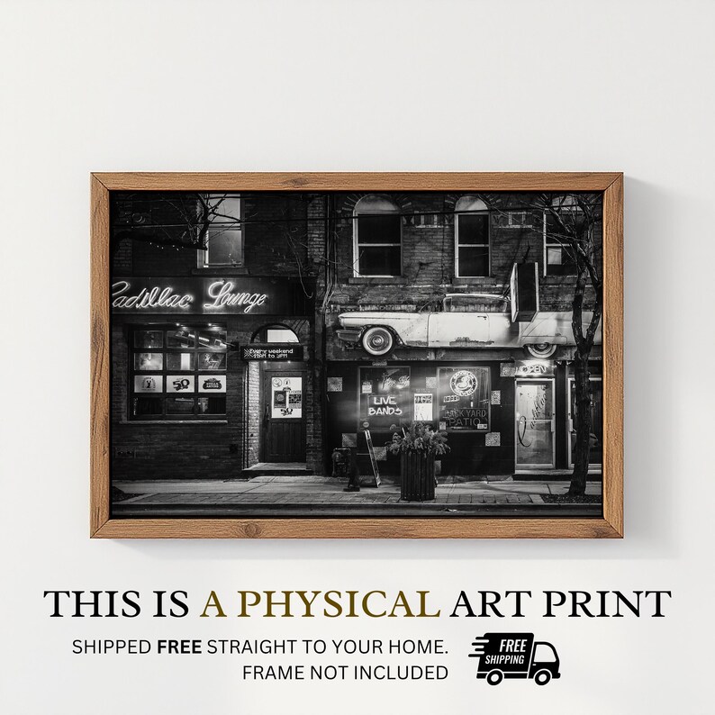 May include: Black and white art print of a building with a vintage car mounted on the side. The sign says "Cadillac Lounge" in neon. The print is framed in a wooden frame. The text at the bottom says "This is a physical art print."