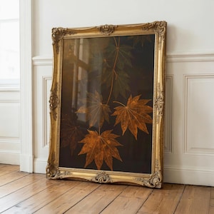 May include: A rectangular wall art piece featuring a dark background with several detailed, golden-brown maple leaves. The artwork is encased in an ornate, heavy gold-colored frame with intricate carved detailing along the edges and corners.