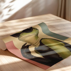 May include: A rolled print featuring a green frog wearing black sunglasses, a multi-strand pearl necklace, and a black sleeveless top. The frog is depicted with one hand raised near its chin, set against a background of muted pink, cream, and teal.