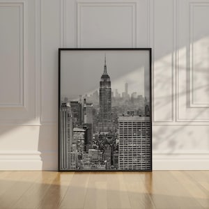 May include: Black and white framed print of the New York City skyline, featuring the Empire State Building as the central focus. The image captures the urban landscape with various skyscrapers and buildings, creating a cityscape.