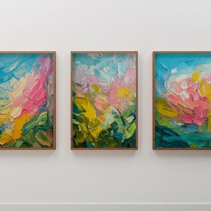 Op de afbeelding: Drie ingelijste abstracte schilderijen in een kleurrijke, impressionistische stijl. De schilderijen tonen een mix van roze, gele, blauwe en groene tinten, wat een levendige en energieke compositie creëert.