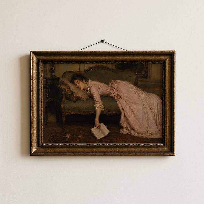 May include: A framed oil painting print depicting a person in a long pink dress reclining on a dark green sofa. The person is resting their head on a pillow while holding an open book that hangs toward the floor. The frame is ornate and metallic gold.