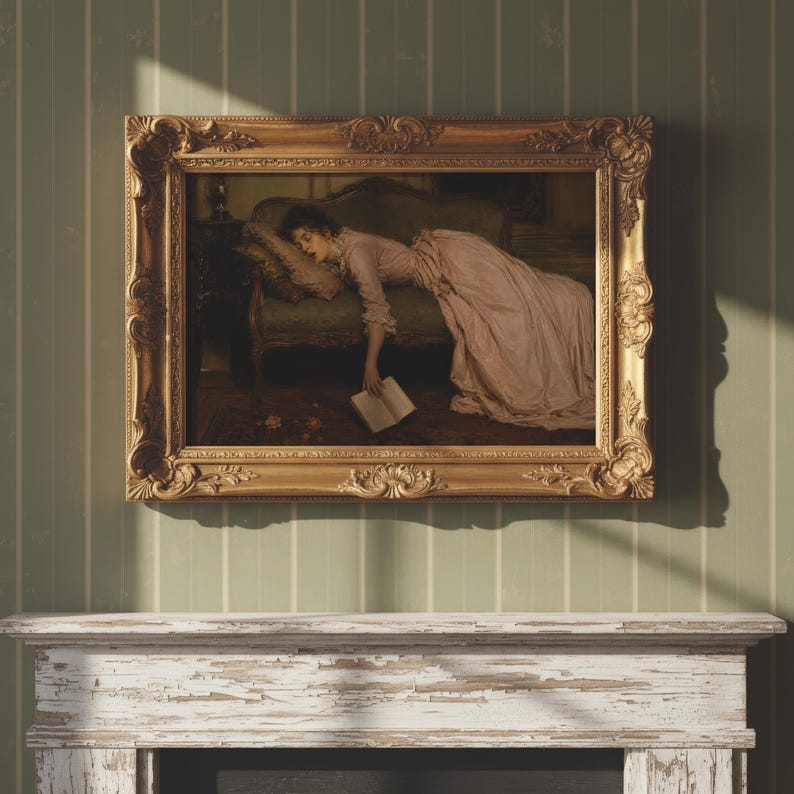 May include: A framed oil painting depicting a person in a long pink dress resting on a green sofa with a book in their hand. The artwork is enclosed in an ornate, heavy gold-colored frame with intricate carved details along the edges.