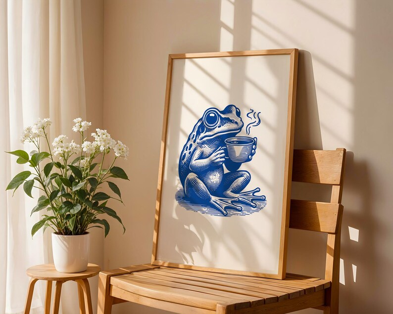 May include: A framed illustration of a blue frog holding a cup of coffee. The frog is sitting on a white background with a light blue shadow. The frame is made of wood and has a white mat.