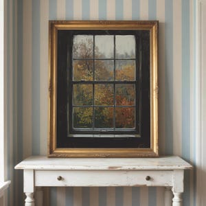 May include: A framed oil painting depicting a view through a dark-paned window looking out onto a landscape with autumn foliage in shades of orange, yellow, and brown. The artwork is enclosed in an ornate, metallic gold-toned rectangular frame.